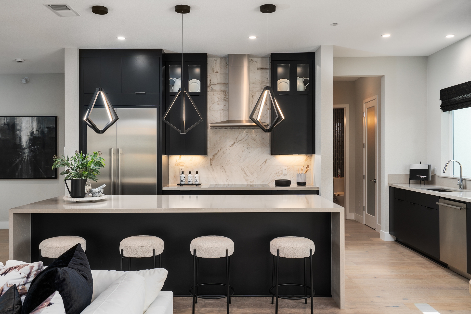 Modern kitchen in City Village, San Ramon featuring black cabinetry, a marble backsplash, unique geometric pendant lighting, and a central island with barstools, designed for contemporary living.